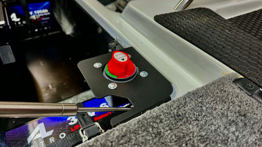 A close-up of a phoenix bass boat trolling motor switch bracket featuring a prominent red emergency stop button on a black mounting plate, set within a gray carpeted compartment.