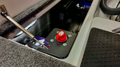 A close-up of a phoenix bass boat trolling motor switch bracket featuring a prominent red emergency stop button on a black mounting plate, set within a gray carpeted compartment.