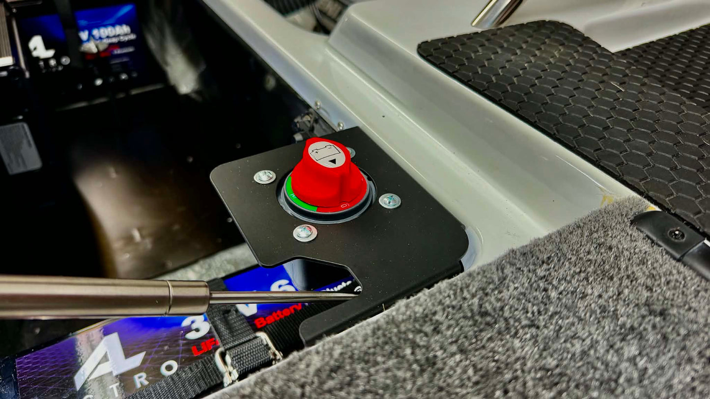 A close-up of a phoenix bass boat trolling motor switch bracket featuring a prominent red emergency stop button on a black mounting plate, set within a gray carpeted compartment.
