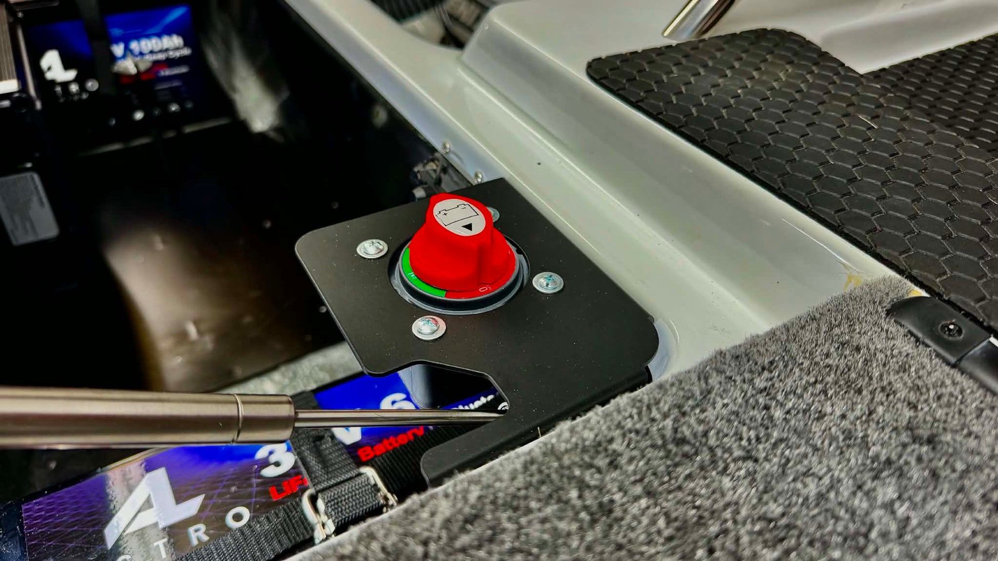 A close-up of a phoenix bass boat trolling motor switch bracket featuring a prominent red emergency stop button on a black mounting plate, set within a gray carpeted compartment.