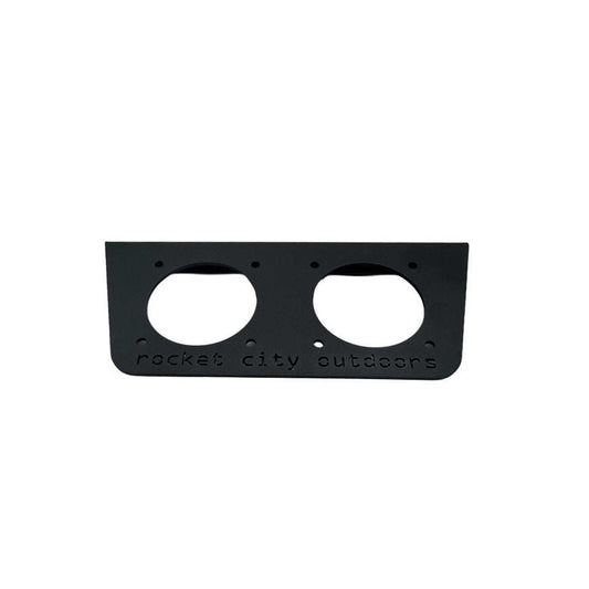 Universal dual battery switch mounting bracket in matte black aluminum, with two circular switch openings and engraved branding